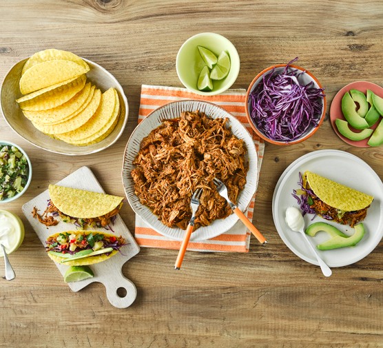 Pulled pork tacos with pineapple salsa A bowl of pulled pork next to avocado, lime wedges, tacos and cabbage