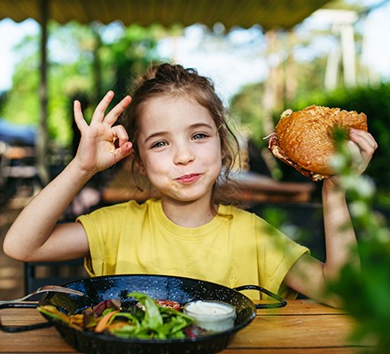 A young girl eating a salad and sandwich looking happy