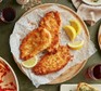 Three breaded chicken Milanese garnished with lemon wedges on a plate