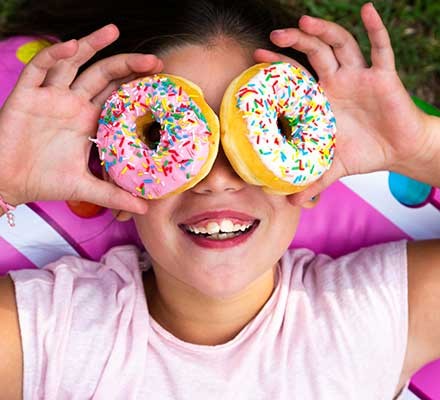A young child holding ring doughnuts over her eyes