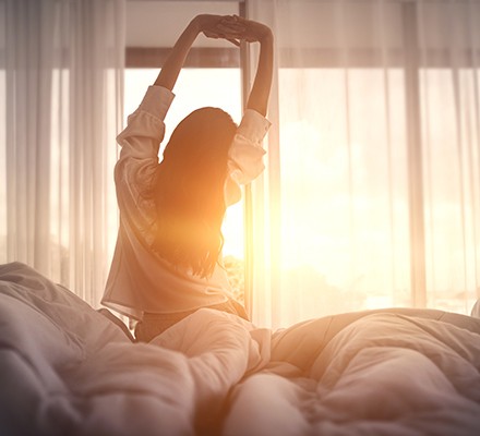 A woman waking up and getting out of bed at sunrise