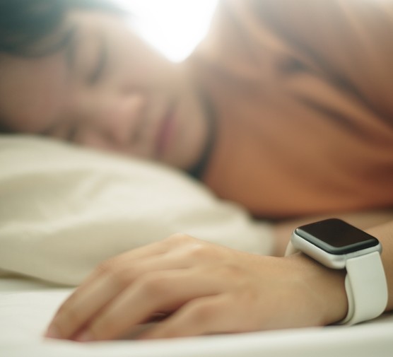 Teenager wearing a smartwatch while asleep on a bed.