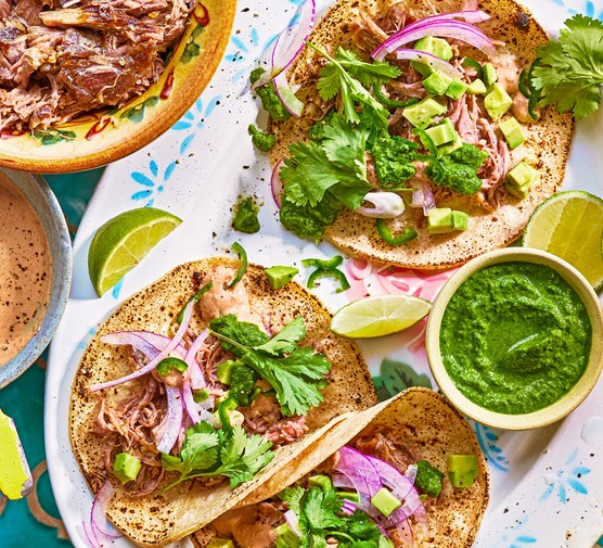 Goat tacos served on a platter with a green sauce