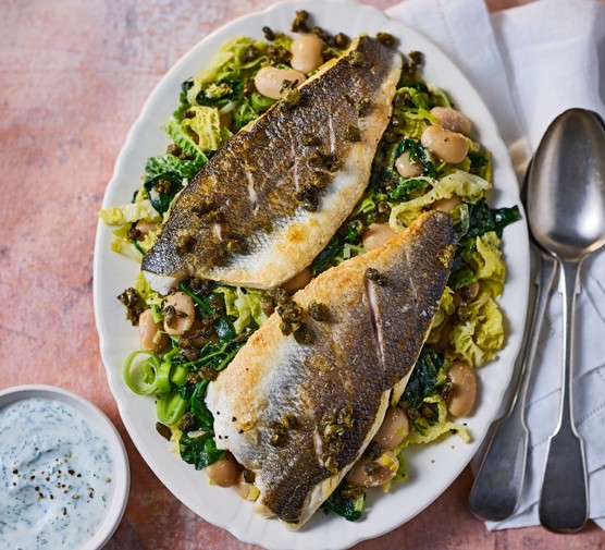 A dish of pan-fried sea bass fillets on a bed of butter beans, spinach, leeks and cabbage