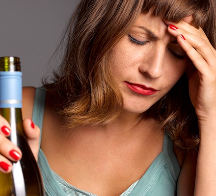A woman with a headache holding a bottle of wine