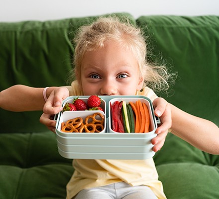 Girl with lunchbox filled with vegetables and berries