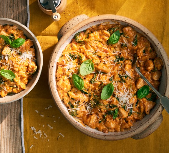 Large pot of orzo garnished with basil and Parmesan, with a portion on the side