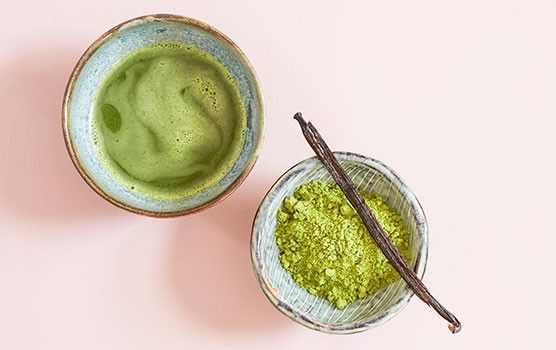 Matcha tea next to a bowl of matcha powder with a vanilla pod on top