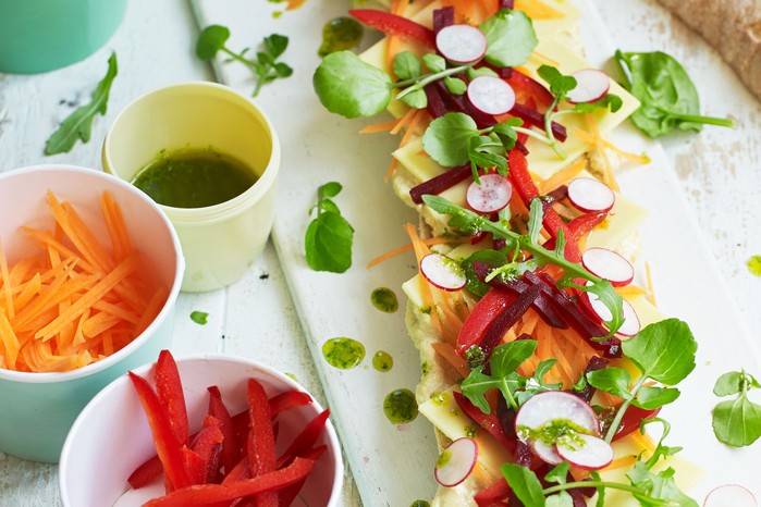 Rainbow baguette Baguette halves topped with colourful veg and cheese, with dips