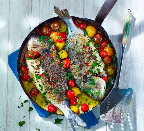 Two whole sea breams in a pan with yellow and red tomatoes.