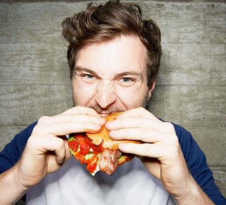 A young man eating a burger looking stressed