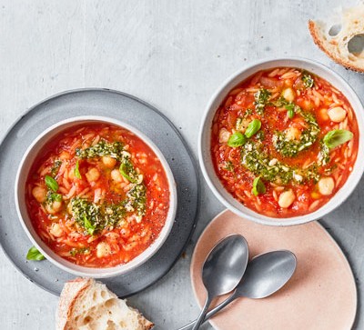 Two bowls of tomato and orzo soup topped with pesto drizzle