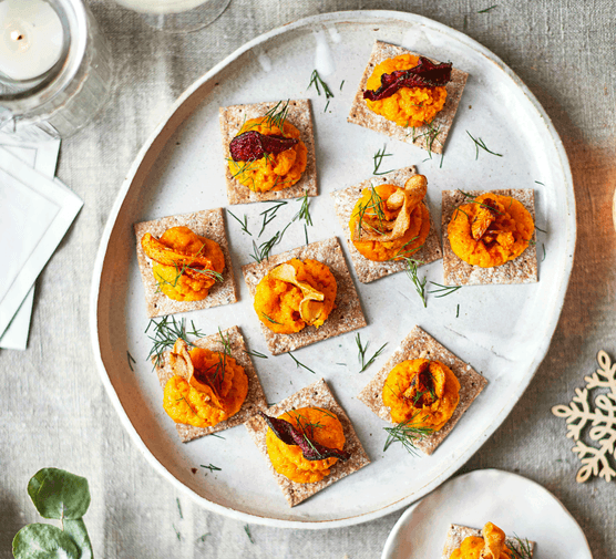 15 budget party finger food ideas Carrot purée on oat crackers on a white serving plate with herbs